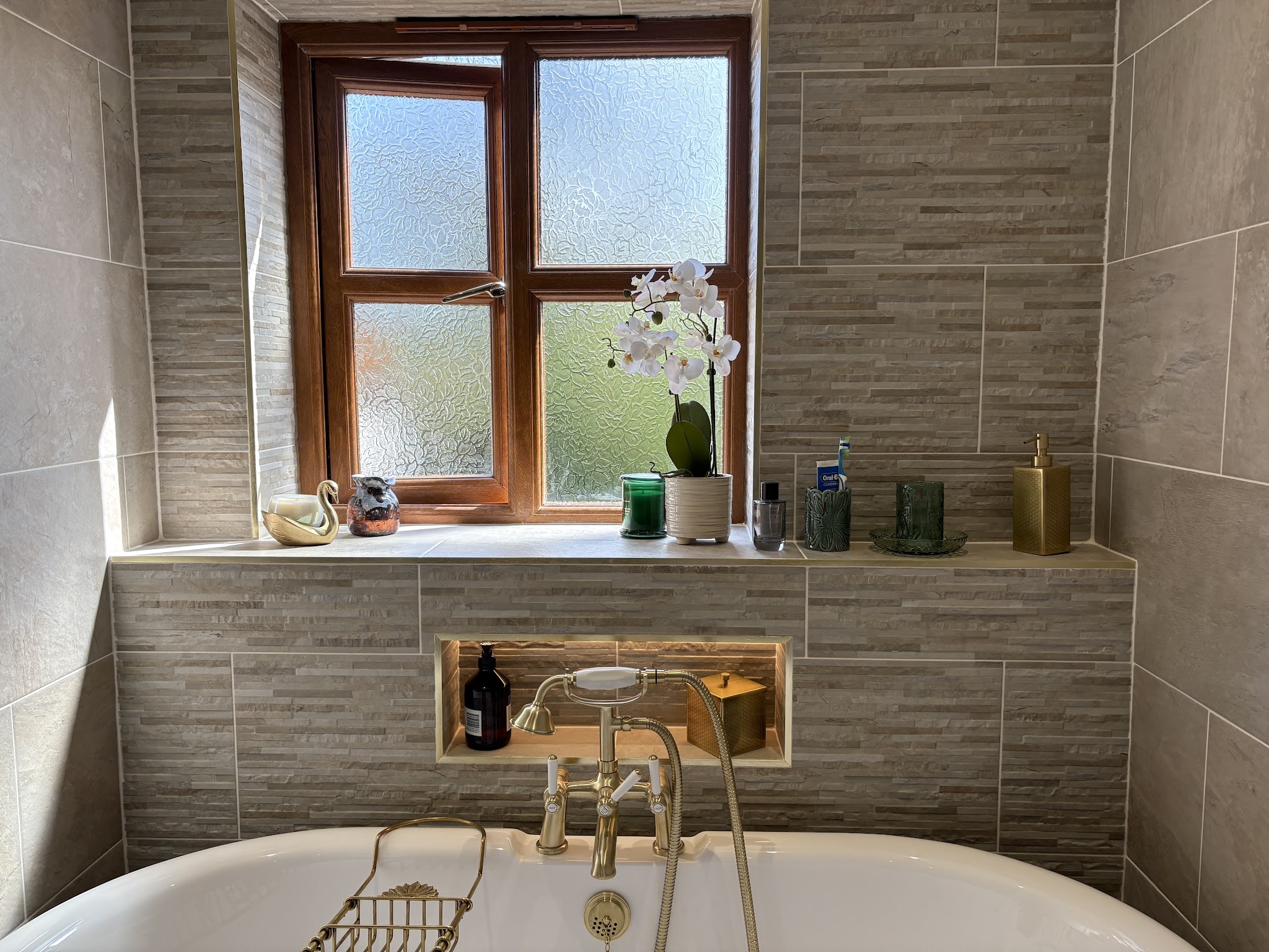 Bathroom with stone-effect tiles and a roll-top bath with brass taps