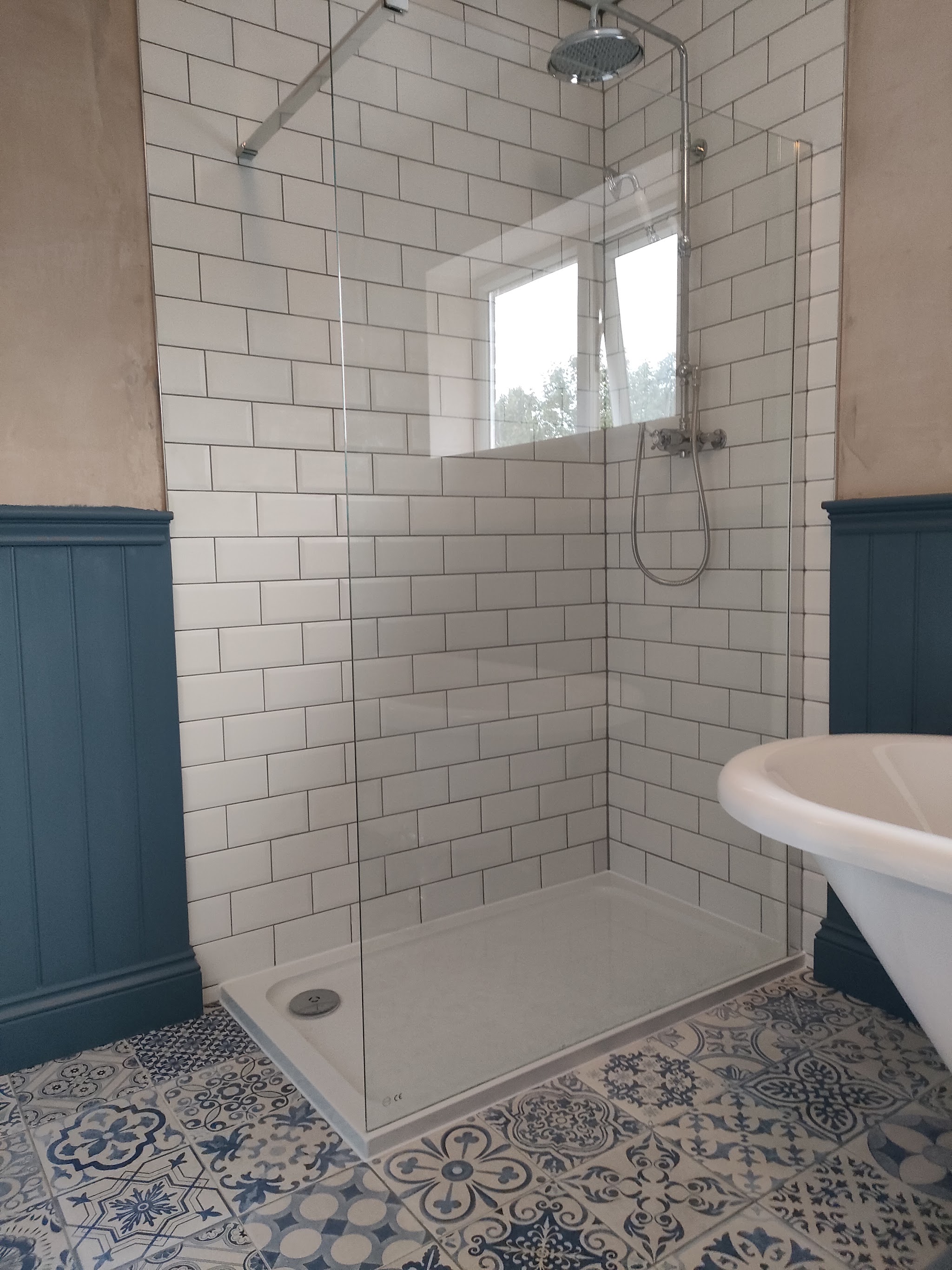 Walk-in shower with white metro tiles and patterned floor tiles beside a roll-top bath