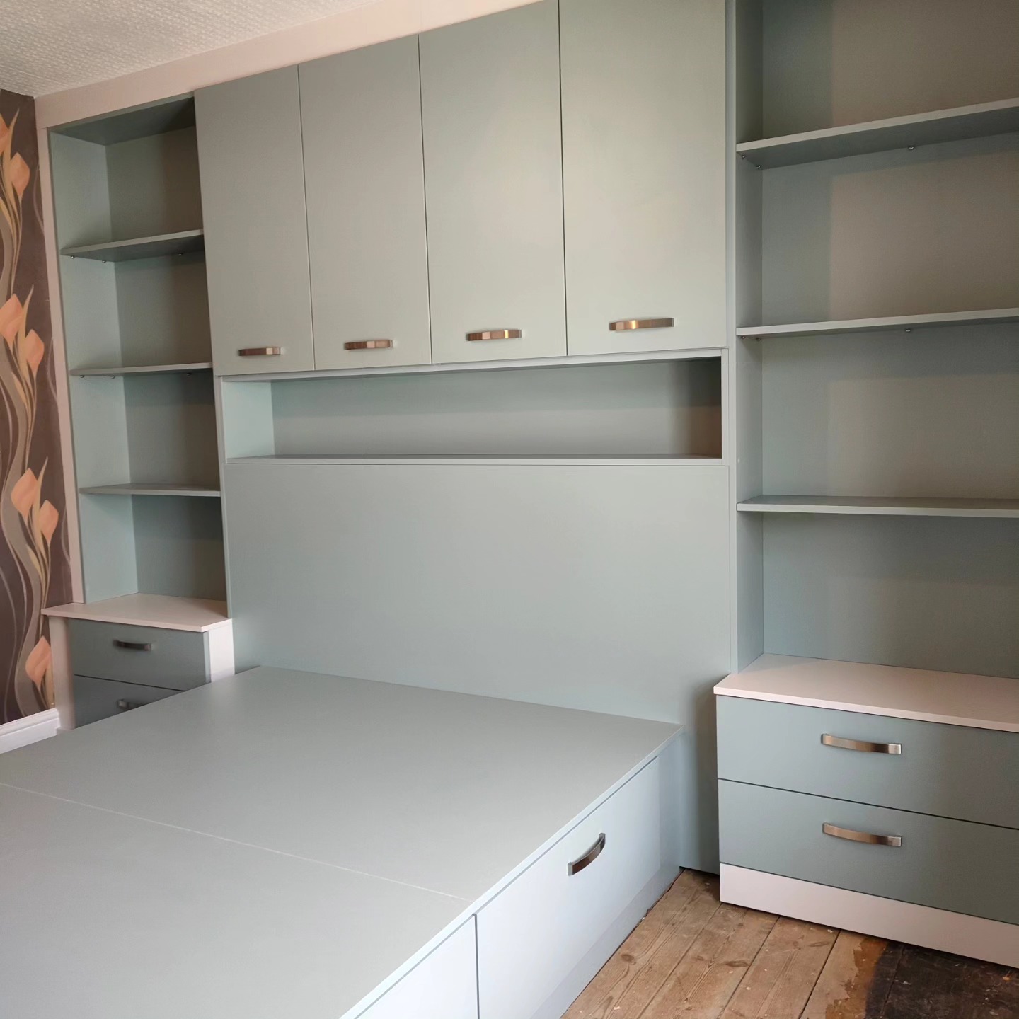 Fitted bedroom furniture in fjord green with shelving around the bed